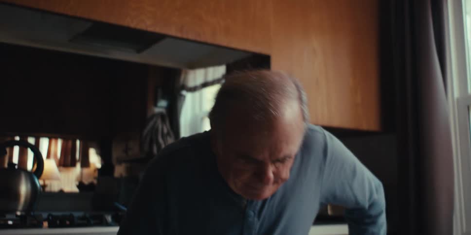 Elderly man walking around the kitchen and sitting down while interacting with his smartphone at the same time