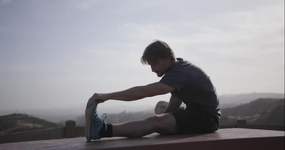 A man is sitting on a picnic table and stretching