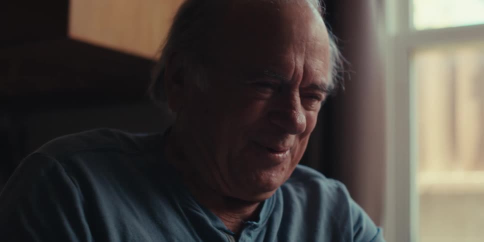 Man sitting indoors is smiling as he is texting on his phone