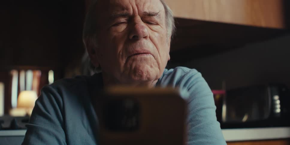 An elderly man with a concerned expression looks at his smartphone