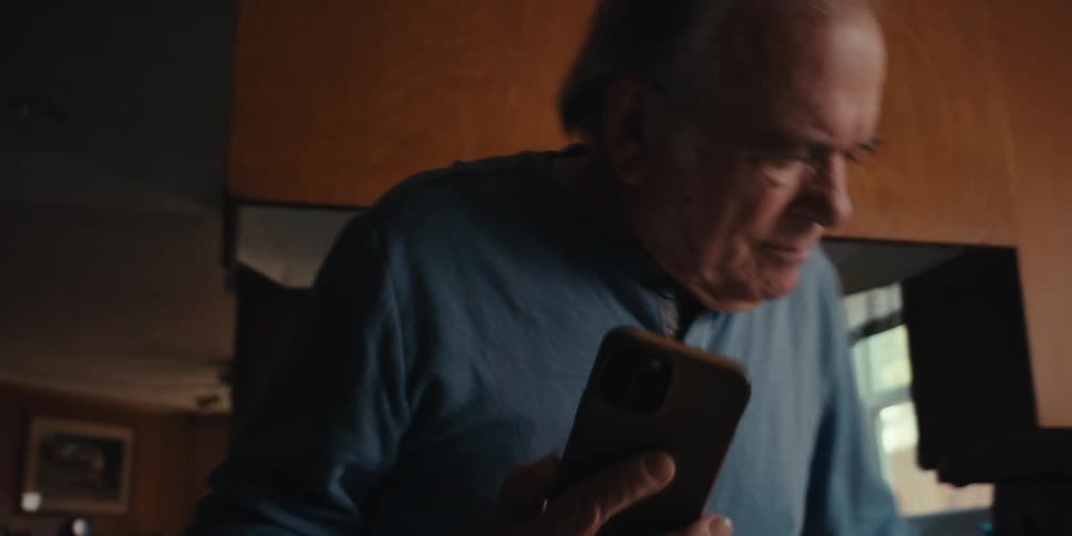 Elderly man walking indoors and sitting down while carrying a smartphone