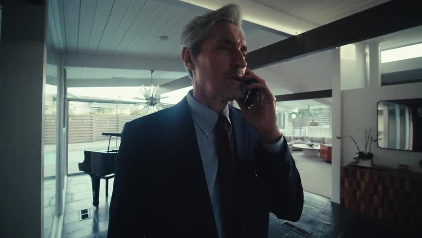 A businessman in a suit talks on the phone with a grand piano in the background of his office