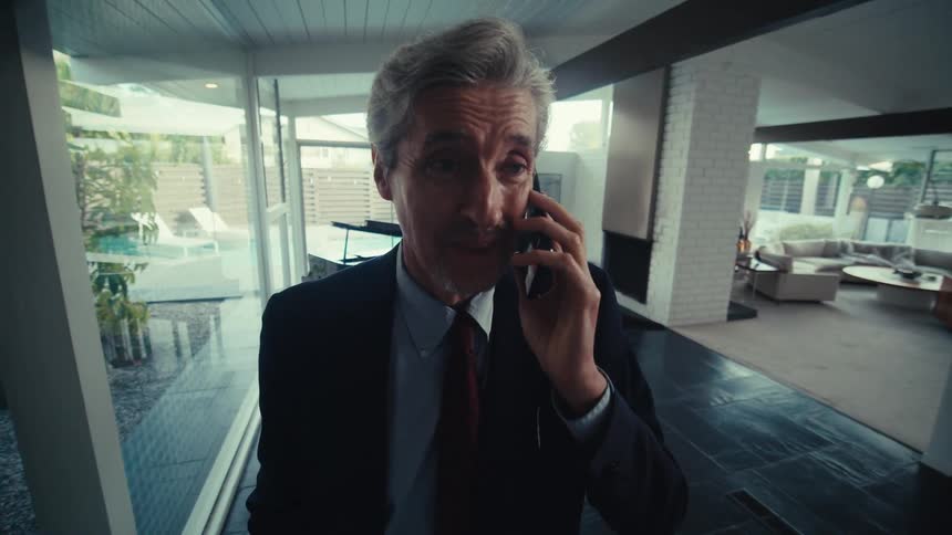 Man is wearing a suit and talking on his cell phone inside his home