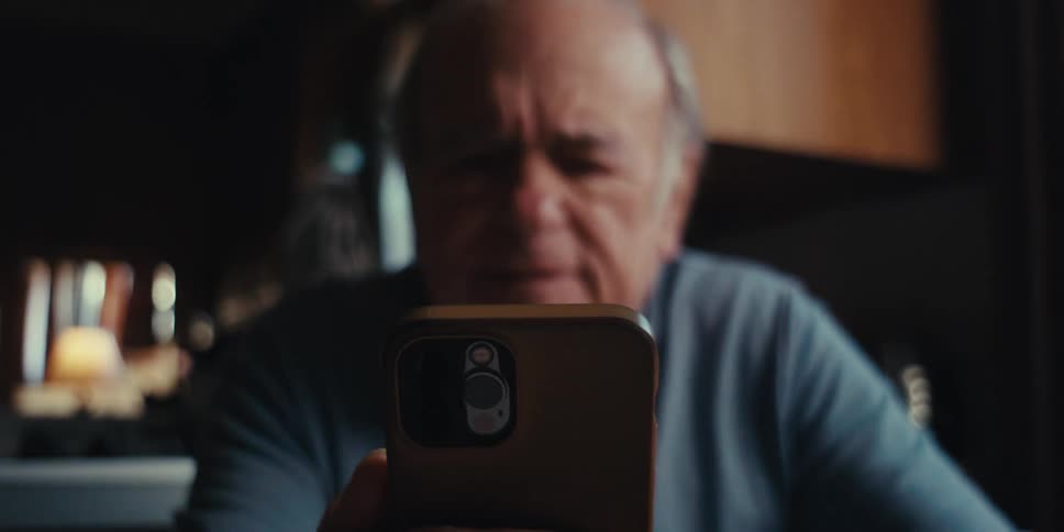 Elderly man walking towards table and sitting down holding smartphone