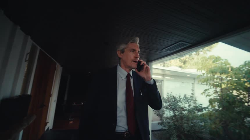 Man walking down hallway of house while talking on cell phone