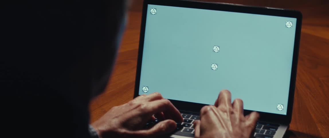 An older man sits at a wooden table and types on his laptop