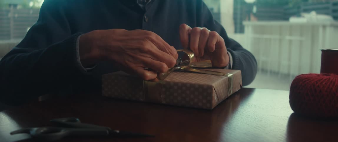 A happy man wrapping a present on a table at home