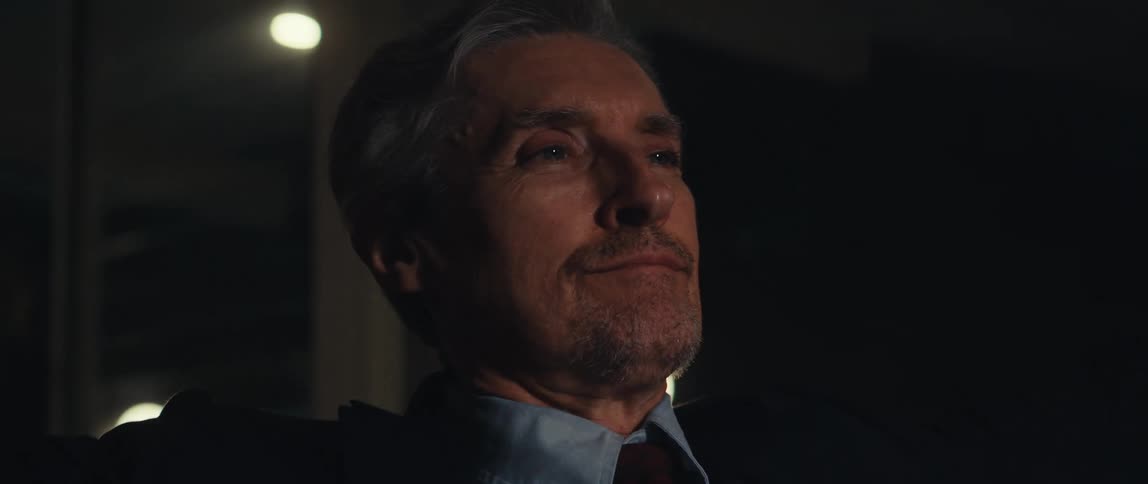 A businessman in a suit uses a laptop and leans back contentedly in his chair at the office at night