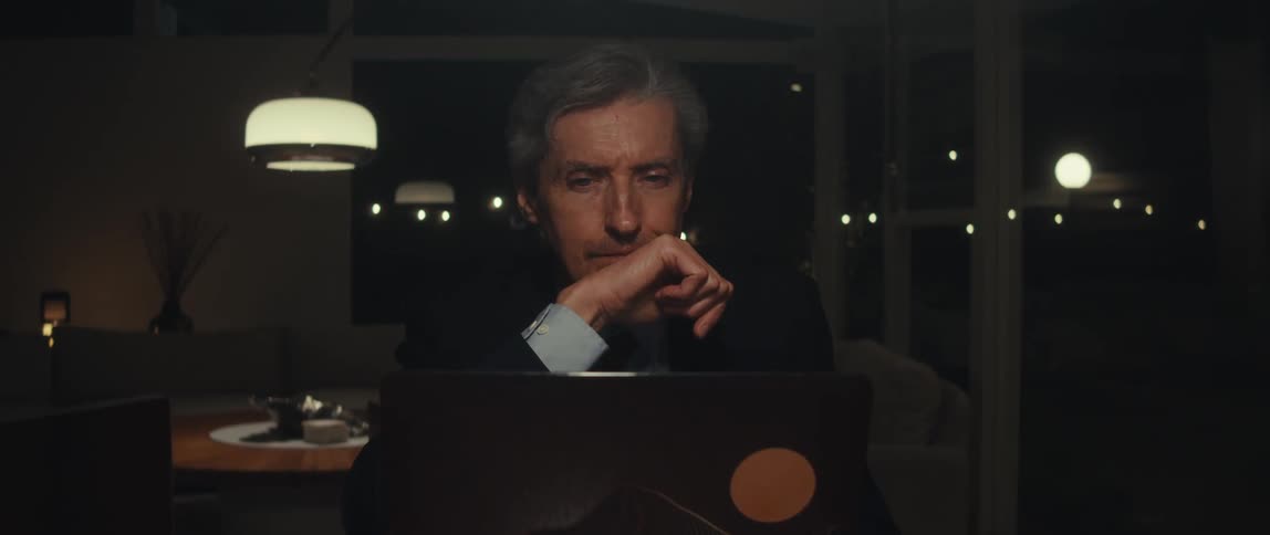 Older man using a computer smiles and nods happily while at home at night