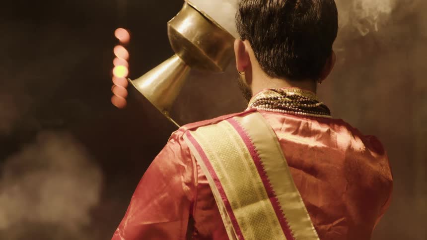 View of a man from behind using a chalice in a ceremony that releases smoke