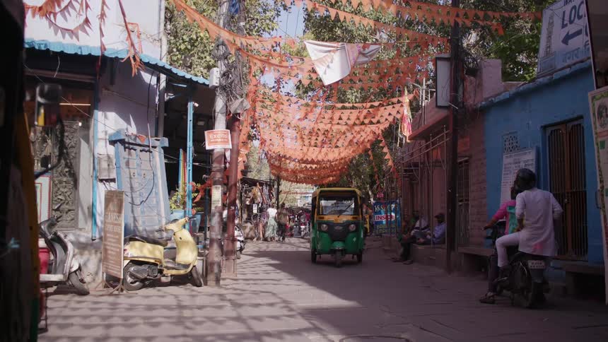 Auto rickshaws drive on a small town street decorated by strings of pennants