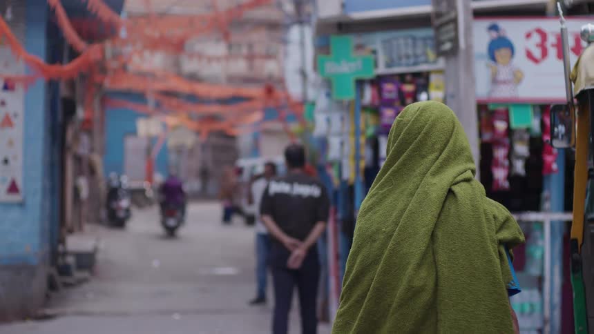 People including one with a green cloth on his head walking down an urban street