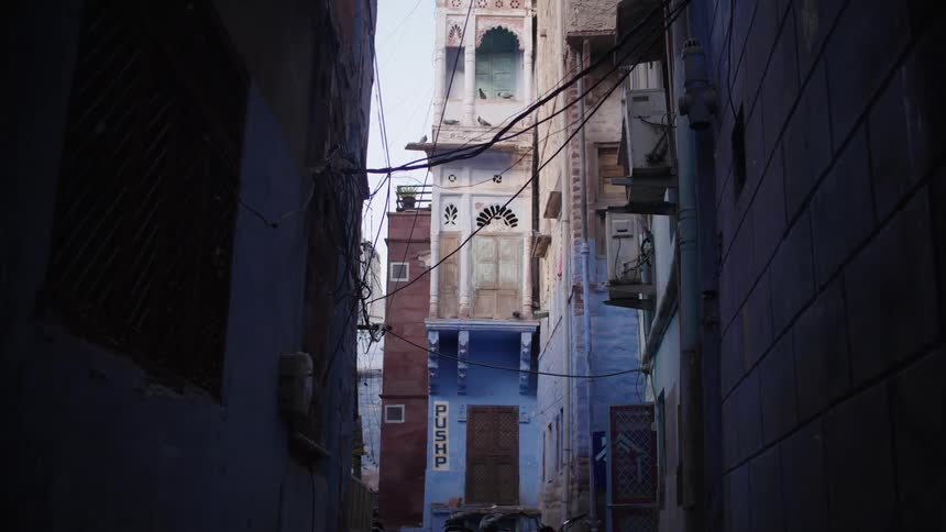 A narrow alleyway between tall buildings with a blue building at the end