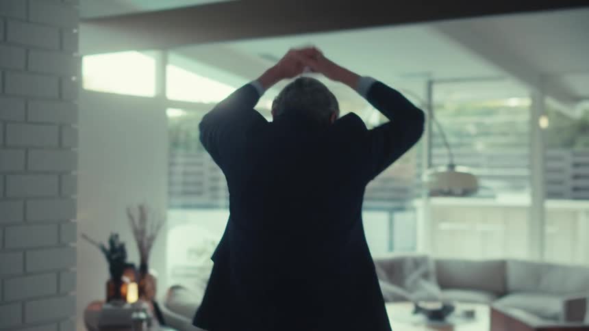 Man in blazer walking around house happily clapping his hands