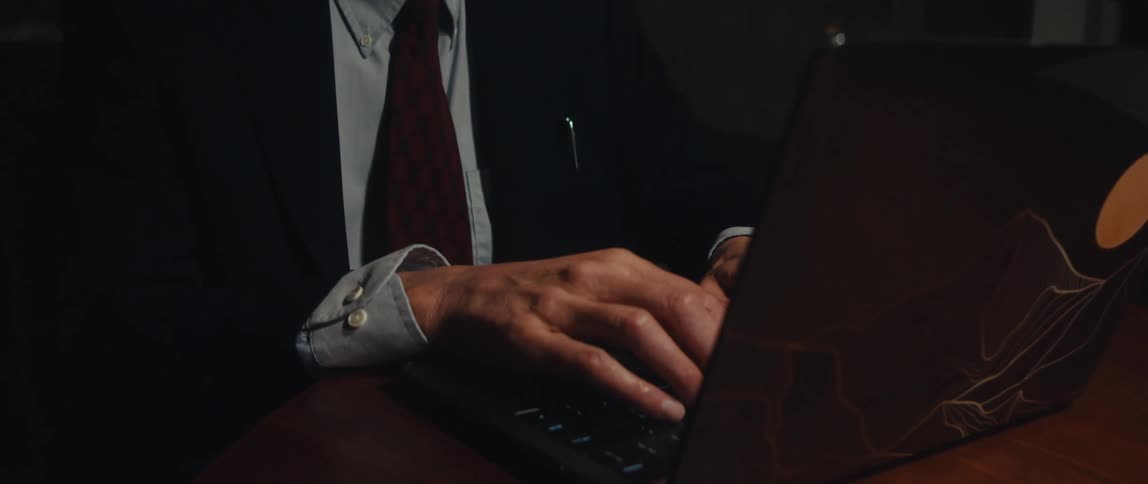 A businessman in a suit types on his laptop keyboard smiling at night in his office