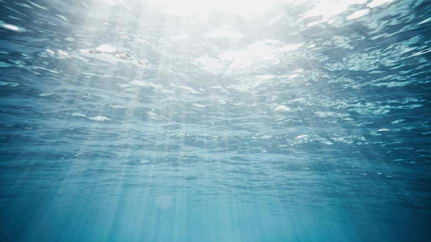 An underwater view of the blue sea with a white light flare coming from the surface