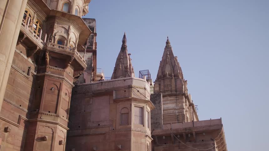 The facade of an old architectural building with some sharp details on the top and a bird passing in the sky