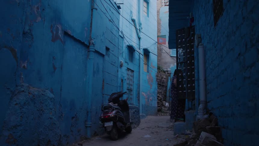 Narrow alley between houses with blue walls and parked motorcycles