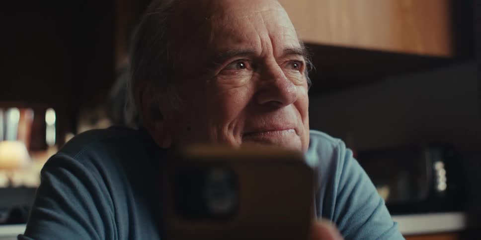 A happy elderly man in a blue shirt uses a smartphone