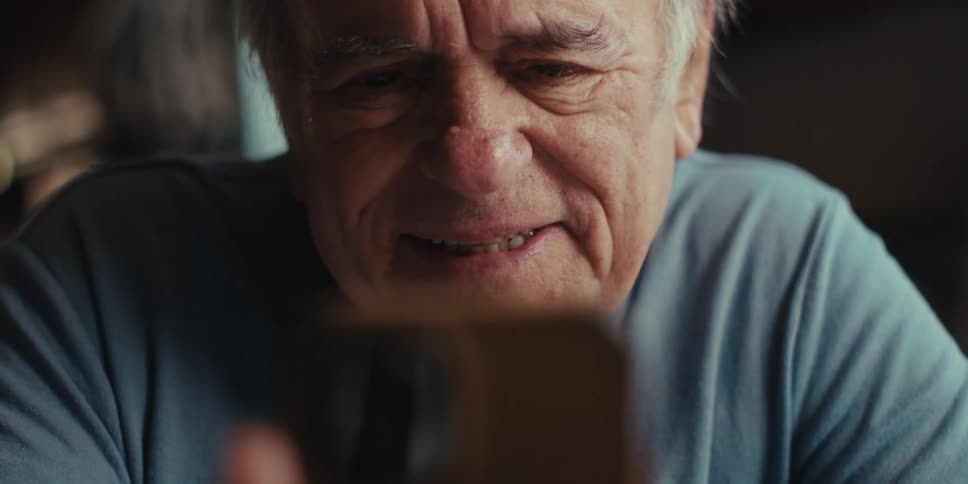 Portrait of an elderly man laughing while using a smartphone