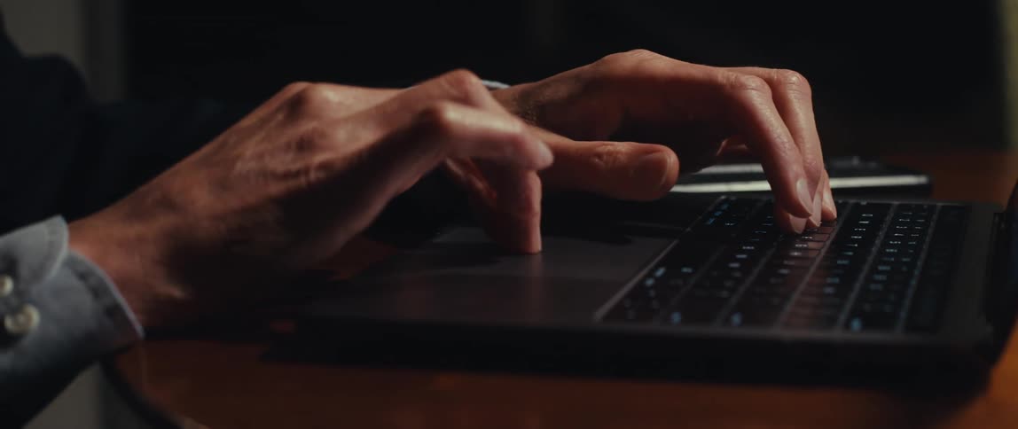 A businessman hands are typing on a laptop keyboard in a dimly lit room