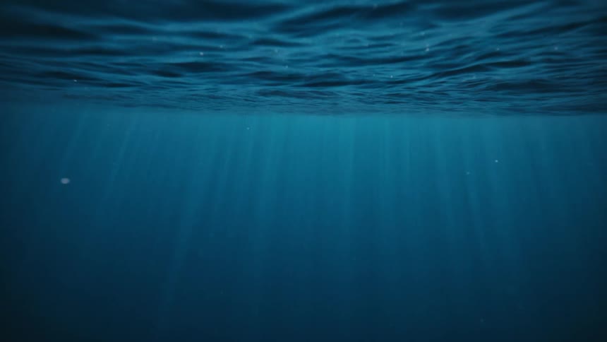 Sunlight streams through the rippling surface of the ocean into the deep blue water below
