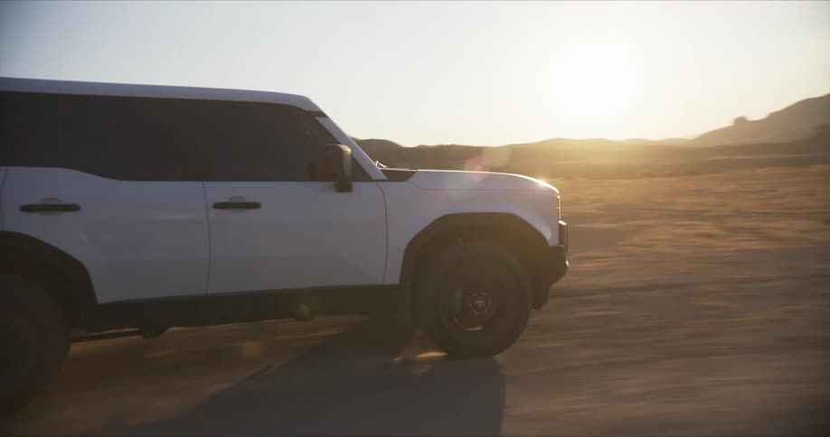 A rugged white suv powers through a dusty desert landscape kicking up sand as it navigates the terrain against a backdrop of distant mountains