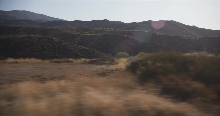 White offroad vehicle speeding down a dirt road with mountains and hills in the background
