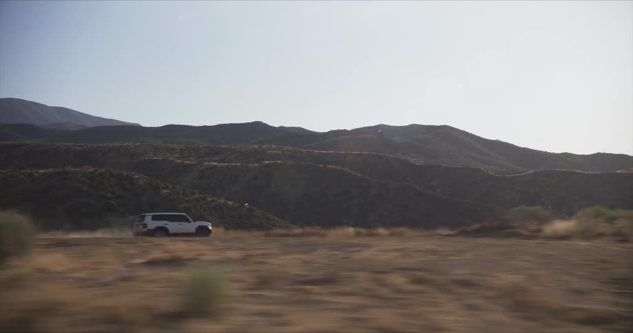 A white suv driving through a dusty desert landscape with mountains in the background