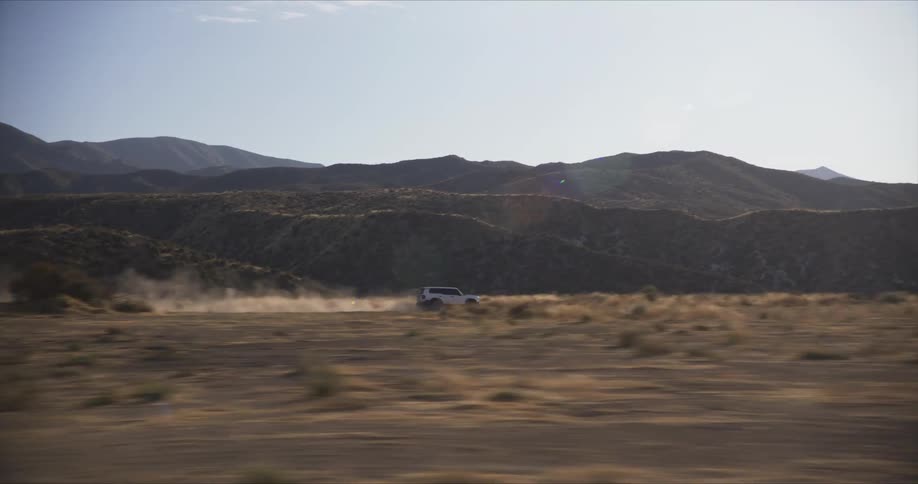A white suv speeds through a desert landscape kicking up a cloud of dust as it navigates the rugged terrain