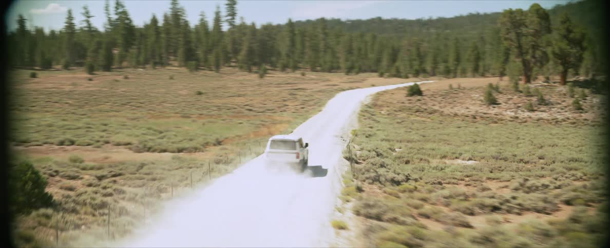 White car traveling at high speed along a dusty trail