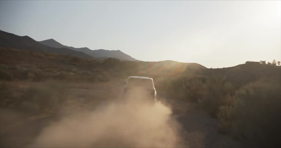 A white suv drives through a dusty desert landscape kicking up a cloud of sand as it navigates the rugged terrain