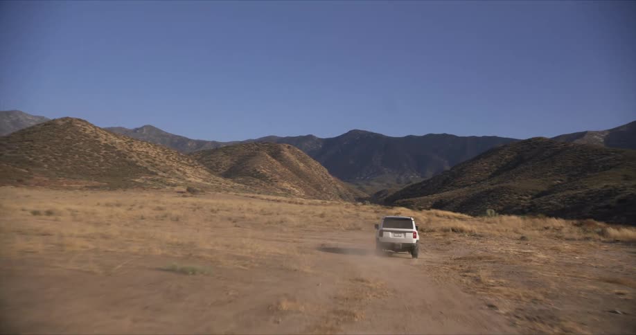 White car traveling on a dirt road surrounded by mountains