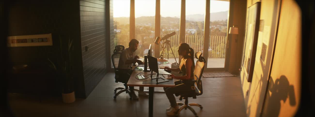Woman sitting down and getting up from an office desk that a man is sitting at