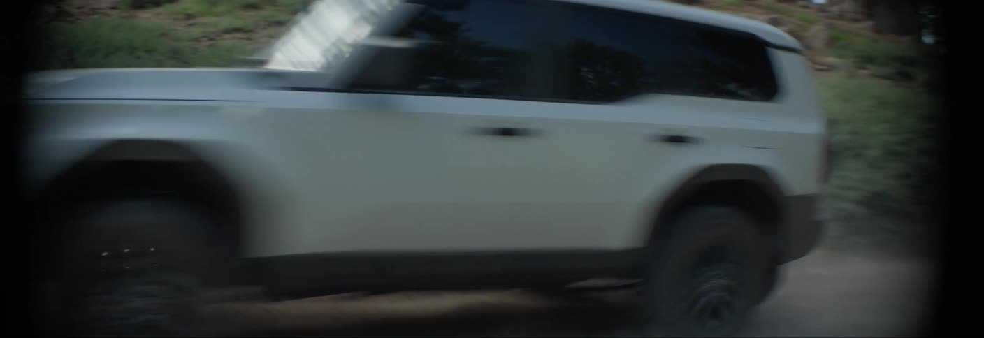 A white suv drives through a dirt road lined with trees and bushes