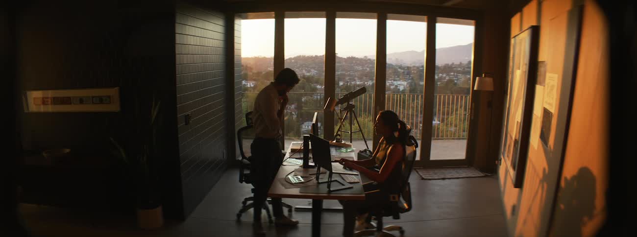 Woman sitting in an office room and a man standing and looking out the window