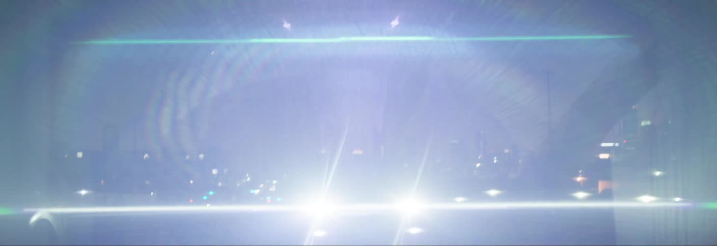 A car driving through a city at night with the headlights illuminating the road and creating a sense of motion and speed