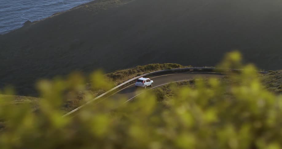 A white car driving along a winding road overlooking the ocean