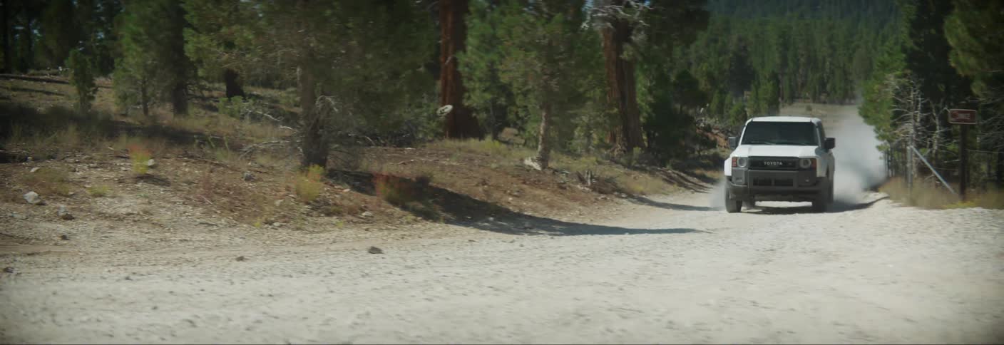 A white suv confidently navigates a dusty dirt road through a dense forest kicking up clouds of dust as it journeys deeper into the wilderness
