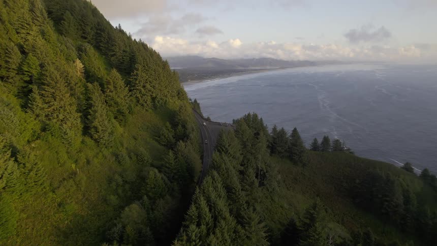 Aerial panorama of a green mountain range with a road with vehicle traffic and the seashore