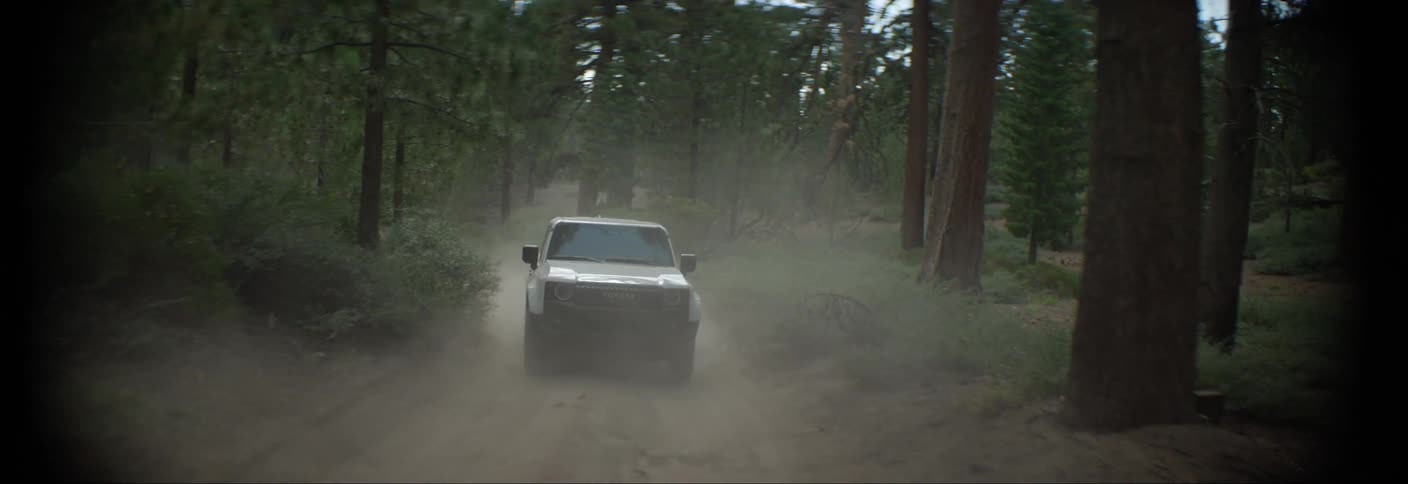 An suv car driving on a dirt road in the middle of a forest and throwing up a lot of dust