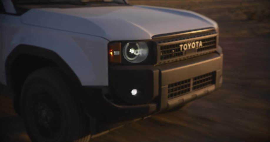 A white suv drives offroad on a dirt path in a dry landscape during sunset
