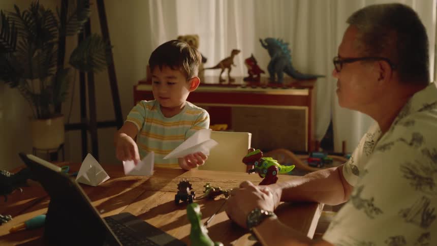 Grandfather sitting with his grandson at the table playing with paper airplanes