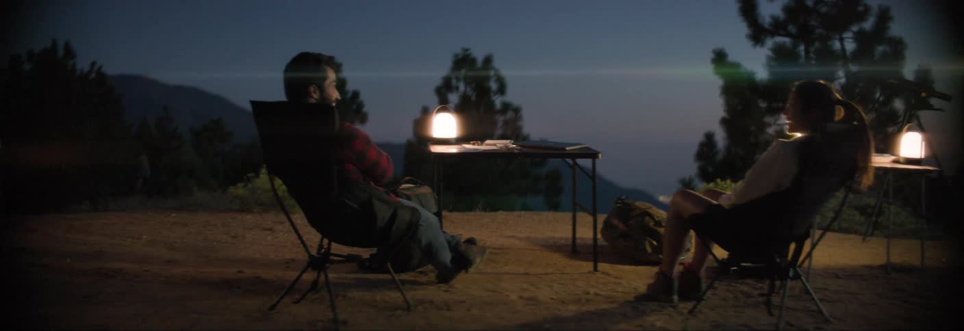 Man and a woman sitting on a chair at a campsite in a natural setting