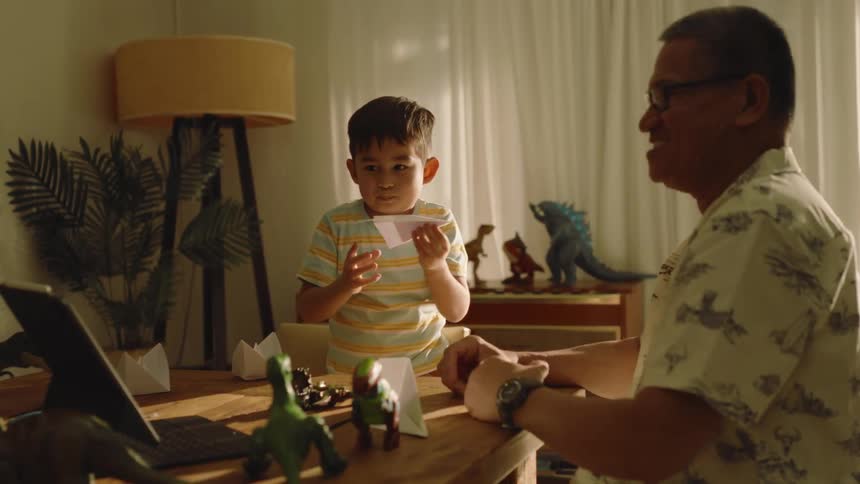 Boy and grandfather playing with paper airplane in living room