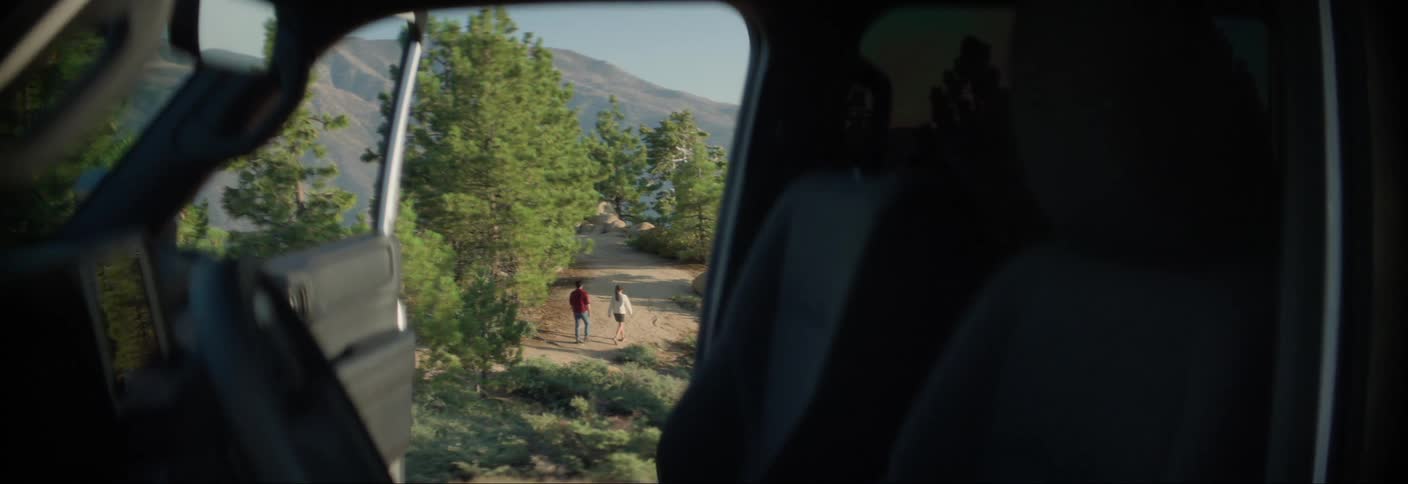 View through a car door of two people walking along a trail