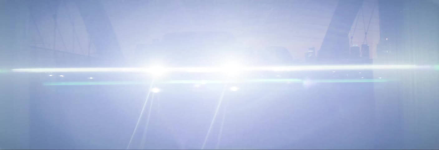 White car crossing a bridge with buildings lit up at night in the background