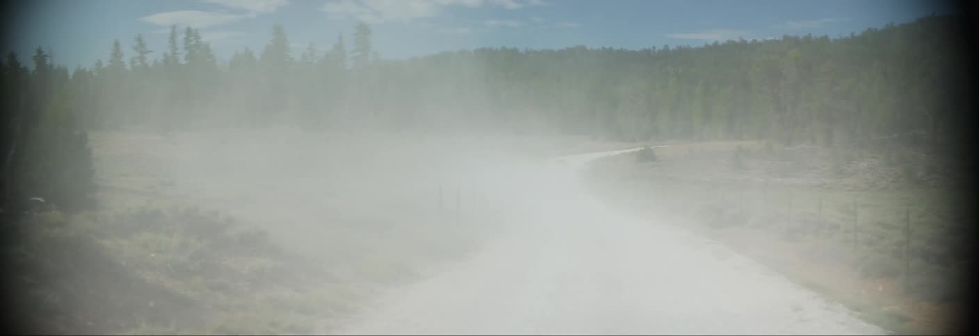 White car speeding down a dirt road spewing dust
