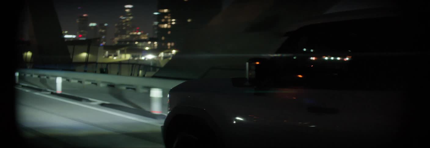 An suv car driving on an asphalt road at night is the background of a metropolitan city with lots of lights