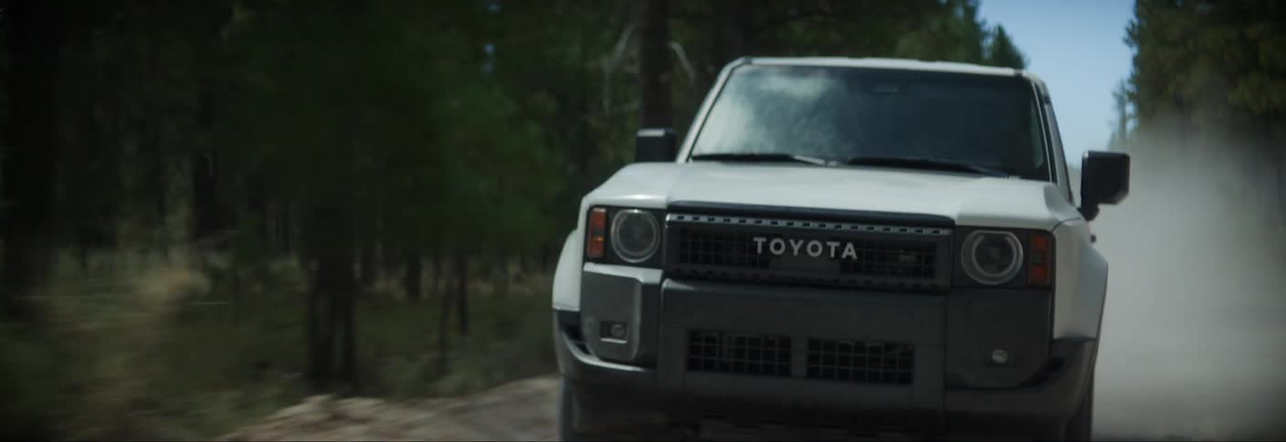 A white suv drives through a dusty forest road kicking up a cloud of dust as it navigates the narrow path
